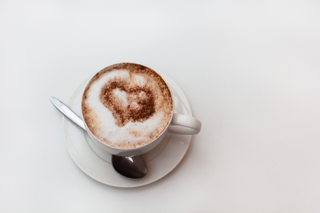 Cappuccino cup on white table background. Foam is decorated with cinnamon heart. Copy space. Top view, located at side of frame. Horizontal. Lactose free concept. Soft focusの写真素材