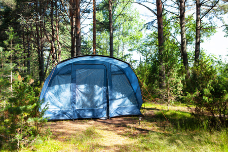 Blue large four-seater camping tent stands in shade of pine forest, weather is sunny. Summer camp, rest, hike. Front view. Horizontalの写真素材