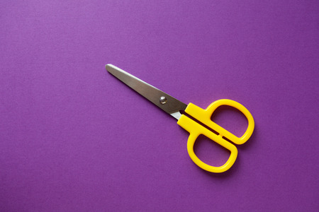 Yellow kid's stationery right-handed scissors on purple papper background. Back to school, DIY...