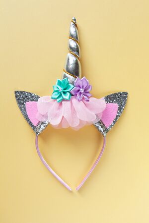 Halloween party accessory, rim with ears and unicorn horn. Pastel yellow background, central composition. Holiday flat lay. Minimal style. Vertical.の写真素材