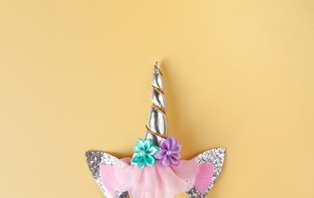 Halloween party accessory, rim with ears and unicorn horn. Pastel yellow background, copy space....