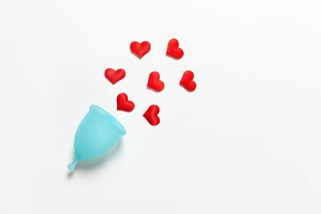 Turquoise menstrual cup on white background with red hearts. Concept zero waste, savings, minimalism, these days. Feminine hygiene product, flat lay, copy space. Horizontalの写真素材