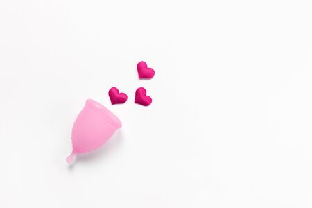 Pink menstrual cup on white background with crimson hearts. Concept zero waste, savings, minimalism, these days. Feminine hygiene product, flat lay, copy space. Horizontalの写真素材