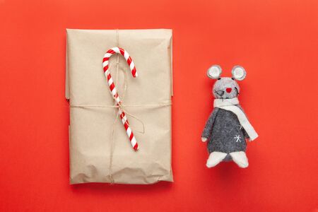 Grey toy rat, symbol of 2020 on Chinese calendar and Christmas gift wrapped in craft paper, decorated with cane candy on red background. Minimal style. Flat lay. Top view. Do it yourself conceptの写真素材