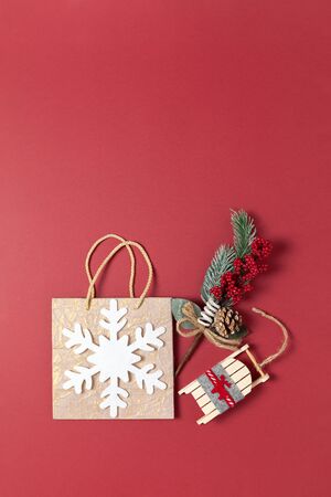 Christmas composition. Golden holiday package with white felt snowflake, bouquet with spruce twig and red berries, toy wooden sled on dark red background, copy space. Vertical, flat lay. Top viewの写真素材