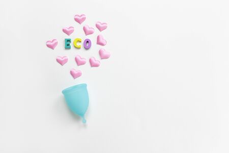 Turquoise menstrual cup on white background with hearts and word Eco from colorful wooden letters. Concept zero waste, savings, minimalism. Feminine hygiene product flat lay, copy space. Horizontalの写真素材
