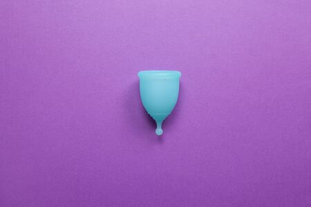 Turquoise menstrual cup on purple background. Concept zero waste living, savings, minimalism, these days. Feminine hygiene product, flat lay, copy space. Horizontalの写真素材