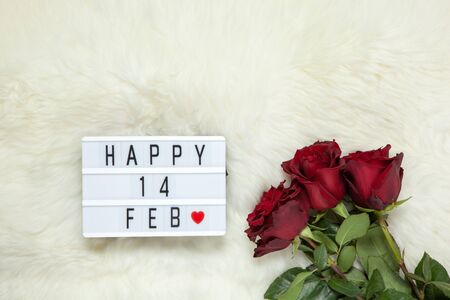 Bouquet of maroon roses on milk white fur carpet, lightbox with inscription Happy 14 FEB that means Valentine's Day. Flat lay. Top view. February 14th celebration concept. Horizontal.の写真素材