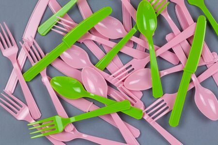 Background from reusable recyclable pink and green forks, spoons, knifes made from corn starch on grey paper. Eco, zero waste, alternative to plastic concept. Flat lay, top view. Horizontal. Closeup.の写真素材