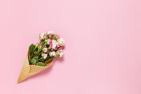 Small roses in waffle cone on pink background, copy space. Minimal style flat lay. For greeting card, invitation. March 8, February 14, birthday, Valentine's, Mother's, Women's day concept. Top view.の写真素材