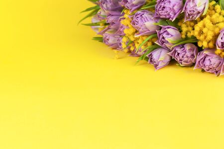 Bouquet of lilac tulips and yellow mimosas on yellow background, copy space, side view, closeup. March 8, February 14, birthday, Valentine's, Mother's, Women's day celebration, spring concept.の写真素材