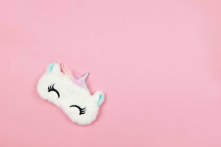 White fluffy fur sleep mask unicorn with closed eyes and small ears on pastel pink paper background, copy space. Top view, flat lay. Concept of vivid dreams. Accessories for girls and young women.の写真素材