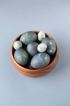 Creatively painted chicken and quail Easter eggs with natural hibiscus dye, look like sea stones in bowl on gray background, copy space. Happy Easter DIY concept. Soft selective focus. Flat lay.の写真素材