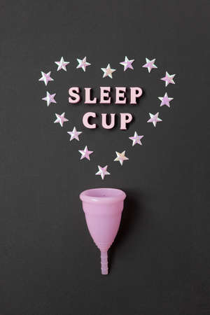 Pink menstrual cup on black background with with heart and words Sleep cup. Concept possibility of use cup at night, zero waste, savings, minimalism. Feminine hygiene product, flat lay. Vertical.の写真素材