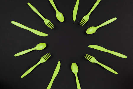 Biodegradable reusable recyclable green forks, spoons, knifes made from corn starch or oats laid out like sun or flower on black background. Eco, zero waste concept. Flat lay. Horizontal. Closeup.の写真素材