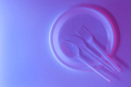 Plastic disposable dishes, plate, spoon, knife, fork on white background in purple and pink neon....