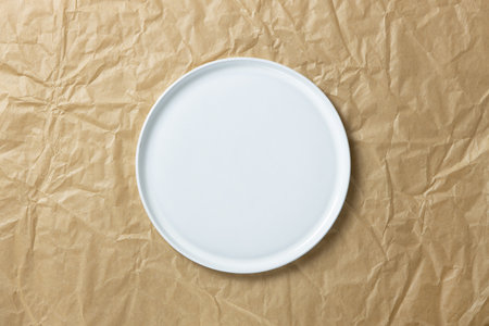 Fashionable blank white round plate with straight edges on crumpled craft paper, minimal style flat...