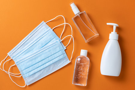 Medical protective, face masks, sanitizer gel, spray, liquid hand soap on orange background, close-up, flatly, minimal. Hygiene concept, protective equipment, prevention of spread of viral infections.の写真素材