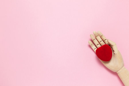 Wooden hand holds red small velvet heart shaped box for jewelry on pink background, copy space, flat lay. March 8, February 14, birthday, Valentine's, Mother's, Women's day celebration concept.の写真素材