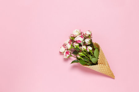 Small roses in waffle cone on pink background, copy space. Minimal style flat lay. For greeting card, invitation. March 8, February 14, birthday, Valentine's, Mother's, Women's day concept. Top view.の写真素材