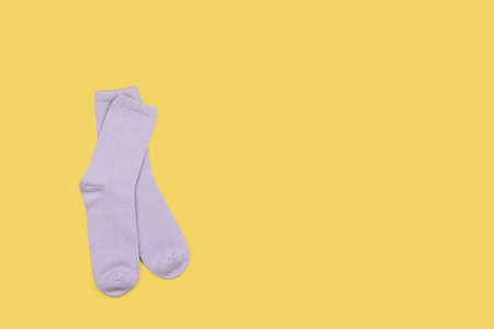 Lilac children's socks without pattern, isolated on yellow background with copy space, flatly, minimal style. Concept kid's clothing, housekeeping, sorting, decluttering, organizing.の写真素材