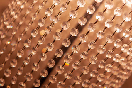 A curtain of transparent glass crystals, decoration on a lamp, close-up, a background of hanging beads. Concept abstract texture, interior details, room lighting. Side view. Diagonal composition.の写真素材