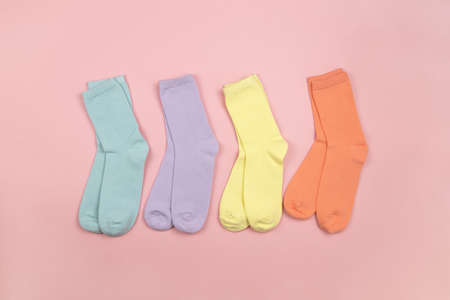 Colored children's socks without a pattern, blue, lilac, yellow, orange on a pink background with a place for text, copy space, flatly, minimal style. Concept for children's clothing, housekeeping.の写真素材