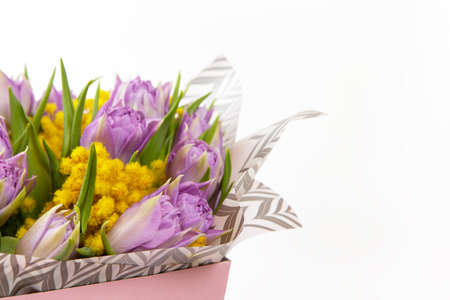 Bouquet of lilac tulips and yellow mimosas in pink box on white background, copy space, side view. March 8, February 14, birthday, Valentine's, Mother's, Women's day celebration, spring concept.の写真素材