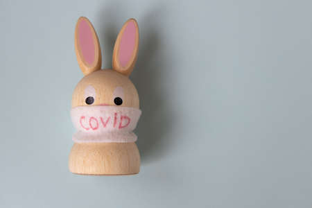 Toy Easter wooden bunny in a medical mask with the inscription  on a gray background. Concept for health, medicine, science, holidays during quarantine, spoiled celebration, restrictions.の写真素材