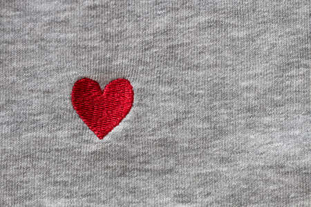 Red heart embroidered with threads on gray fabric background. Close-up, macro, copy space, flat lay. March 8, February 14, birthday, Valentine's, Mother's, Women's day celebration concept, love.の写真素材