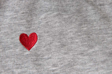 Red heart embroidered with threads on gray fabric background. Close-up, macro, copy space, flat lay. March 8, February 14, birthday, Valentine's, Mother's, Women's day celebration concept, love.の写真素材