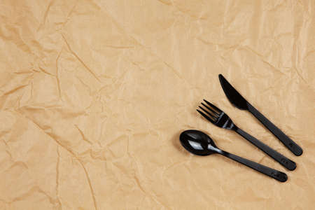 Reusable recyclable black fork, spoon, knife made from corn starch on brown crumpled craft paper, copy space. Eco, zero waste, alternative to plastic concept. Flat lay. Horizontal. Close-up.の写真素材