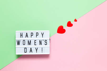 Light board with inscription Happy Women's Day, three red different-sized hearts on pastel...