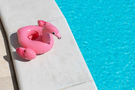 Inflatable pink flamingo near swimming pool on bright sunny day, copy space. Concept summer vacation, entertainment, water, air, sunbathing, health. Top view. Horizontal. Soft selective focus.の写真素材
