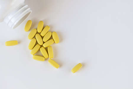Yellow long vitamins lying next to pill jar on white background, macro, close-up, copy space. Nutritional supplements concept, health, vitamins, trendy color of 2021, Illuminating. Horizontal.の写真素材