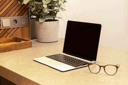 Workplace in apartment or cafe with modern interior. Open laptop and glasses on the table top. Business concept, remote work from home, distance learning, use of technology. Place for text, layout.の写真素材