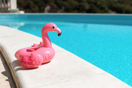 Inflatable pink mini flamingo, cocktail stand near swimming pool on bright sunny day, copy space. Concept of summer vacation, entertainment, water, air, sunbathing, health. Side view. Horizontal.の写真素材
