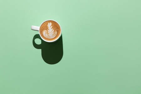 Blank white mug with cappuccino, latte design in hard light on pastel green background, top view, flat lay. Mockup for design. Minimal style. Concept hot drinks, beverages, vegetable milk. Horizontal.の写真素材