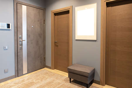 Modern entrance hallway in neutral shades of brown and gray tones. On wall there is photo frame with mockup, front door with intercom. Concept fashionable interior design, use of natural materials.の写真素材