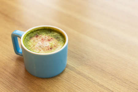 Blue cup with green tea matcha latte, with freeze-dried strawberries on a wooden table, copy space. Healthy nutrition concept, drinks with vegetable or cow's milk, vegan beverages. Place for text.の写真素材
