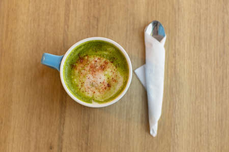 Blue cup with green tea matcha latte, with freeze-dried strawberries, spoon on wooden table, copy space. Healthy nutrition concept, drinks with vegetable or cow's milk, vegan beverages. Place for text.の写真素材