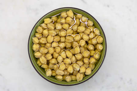 Chickpeas soaked in water, in bowl, on marble table. Concept of healthy eating, veganism, vegetarianism, meat and egg replacement. Prepare chickpeas before making hummus and other legume dishes.の写真素材
