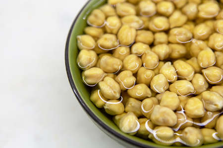 Chickpeas soaked in water, in bowl, on marble table. Concept of healthy eating, veganism, vegetarianism, meat and egg replacement. Prepare chickpeas before making hummus and other legume dishes.の写真素材
