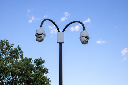 Surveillance cctv (closed circuit television) camera installed in public park on blue sky background for protection against crime, observation of people, control of observance of public order.の写真素材