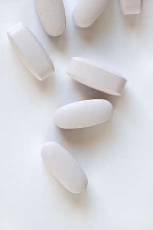 White or light gray long vitamins or pills on white background, macro, close-up, copy space, flatly. Nutritional supplements concept, health, vitamins, monochrome minimal style. Vertical.の写真素材