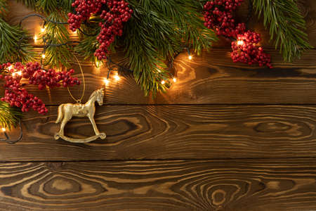 Christmas background. Nobilis fir branches, twigs with red berries, toy golden horse on brown wooden planks. Copy space, flat lay, top view. Holiday, Xmas, New Year concept. Mockup.の写真素材