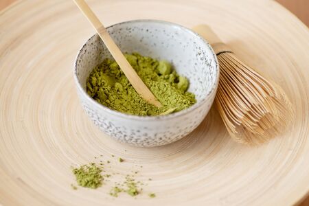 Green tea matcha dry powder in grey bowl with Japanese tools whisk and spoon on light brown babmoo wooden plate. Superfood healthy nutritious food concept, vegetarian vegan dietの写真素材