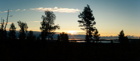 A breathtaking sunrise illuminates the Nordic wilderness, casting golden light over silhouetted...
