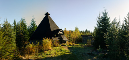Rustic wooden kota shelter with steep conical roof stands harmoniously in lush autumn forest bathed...