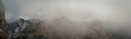 Panoramic mountain landscape shows jagged Dolomites peaks fading into dense low clouds near Punta...